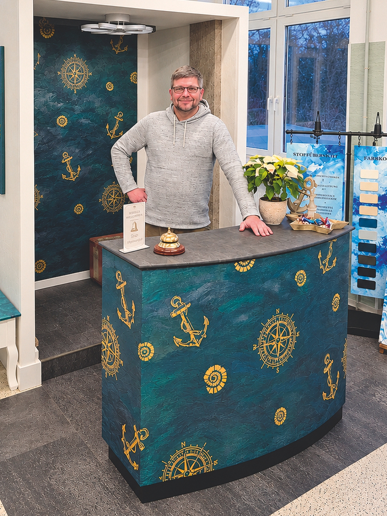 Das Meisterstück des Maler- und Lackierermeisters Marcel Kaiser. Zu sehen ist ein Empfangsbereich mit dekorativer Wand- und Oberflächengestaltung in maritimem Design mit goldenen Ankern und Steuerrädern auf blauem Hintergrund.