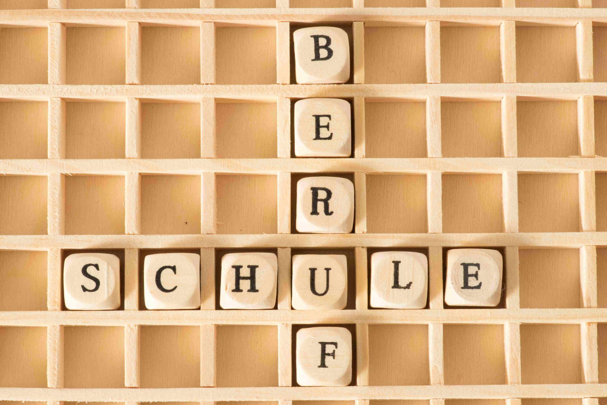 Holzbuchstaben in einem Setzkasten bilden waagerecht das Wort „SCHULE“ und senkrecht das Wort „BERUF“.
