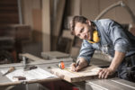 Tischler in seiner Werkstatt arbeitet an einem Holzstück und lächelt in die Kamera
