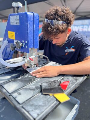 Handwerkskammer Halle Eine Person arbeitet konzentriert an einer Steinsäge, auf deren Tisch mehrere farbige Materialstücke liegen.